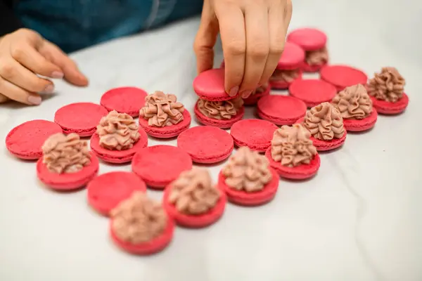 Røde Stykker Makroner Ligger Hvidt Køkkenbord Hver Med Beige Creme Royaltyfrie stock-billeder