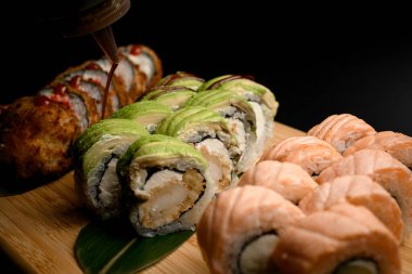Üç suşi seti pirinç, somon, krem peynirli tempura, yılan balığı, karides, ahşap bir tahtanın üzerinde soya sosuyla sulanan deniz ürünleri.