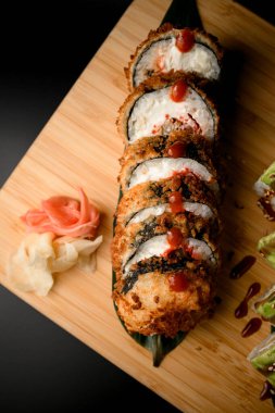 Kahverengi soslu, turşulu, pembe zencefilli ve beyaz pirinçli Norveç suşisine sarılmış. Siyah arkaplanda tahta büyük bir tahta.