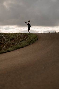 Bulutların arasında sırıtarak, uzun tahtasını kaldırır, karamsar gökyüzünün altında neşeli bir anı yakalar..