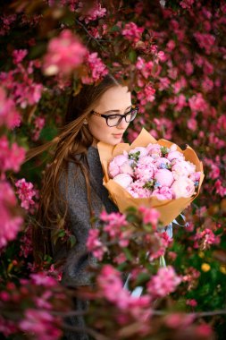 Uzun kırmızı gül çalılarının arasında, kahverengi saçlı ve gözlüklü bir kadın, ona verilen düşünceli bukete hayran..