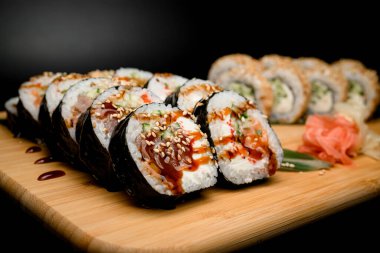 Ton balığı, somon, salatalık ve tobiko havyarlı ruloların yer aldığı resim sahnesi gözler önüne seriliyor. Arka planda, zencefil ve wasabi eklenmiş susam tohumları serpiştirilmiş klasik bir set ve