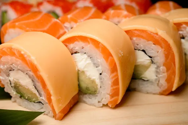 Dive into a unique experience with salmon rolls, each adorned with a slice of cheese, nestled among a diverse array of sushi sets.