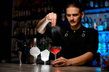 Barmen bir parça lezzet sıkıyor, kokteyl bardağının üstünde tutuyor, böylece sıçramalar farklı yönlere uçuyor, yakınlardaki barda başka kokteyl ekipmanları var.