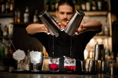 Barmen bardağın son damlasını bardağın iki yarısından bardağın iki yarısına döker ve tezgahın üzerinde süzgeçler durur.