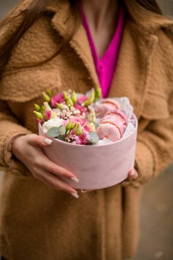 Yumuşak bir kutuda pembe badem kurabiyesi ve çiçeklerle narin elleri açık bir alanda duruyor.