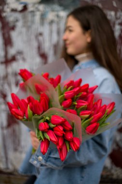 Bouquet of wonderful sweet tulips on the shoulder of a long hair girl in a denim shirt on a blurred background clipart