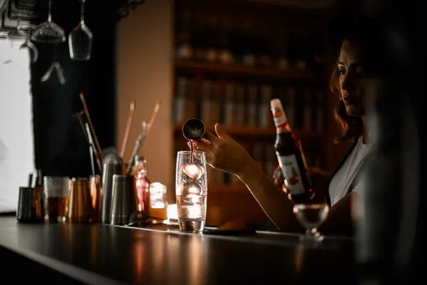 stock image Female bartender pours pink drink from jigger into glass with three ice cubes, selective focus