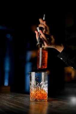 Siyah gömlekli alkollü kokteyl üreticisi barın üstünde viski, rom veya konyak ve buz ile elit bir alkol kokteyli yapar.