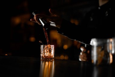 Kokteyl ustasının elleri, barın karanlık arka planında bardakta güçlü bir alkolik içkisi.