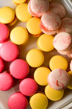 Büyük bir cam kasede bej, beyaz, koyu pembe ve sarı renkte krema ile çok renkli makaronların karışımı.