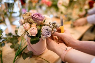 Çiçekçinin elleri, ahşap bej masanın üzerinde duran profesyonel güzellikte taze çiçekler oluşturur.