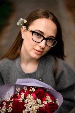 Koyu renk saçlı, gözlük takan güzel bir kızın portresi ve bir buket güzel çiçekli gri bir ceket.