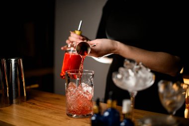 Kokteylleri karıştırmak için bardağa kahverengi sıvı dolduran bir barmenin kadın elleri. O da gayzer şişesinden döktü. Seçici odak, bulanık arkaplan