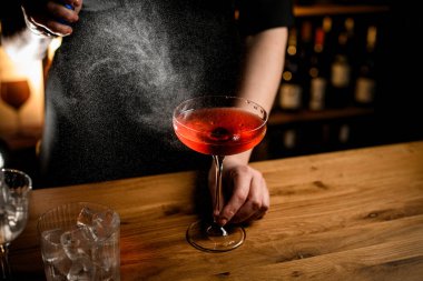 Kadın barmen, bardağa kahverengi soğuk kokteyl sıkar. Yanında buz küpleri olan bardaklar durur.