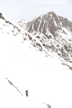 Kayakçı dik bir dağ tırmanışının üstesinden gelir, karlı bir yamacın arka planına karşı ve hemen hemen karla kaplı bir dağ zirvesine.