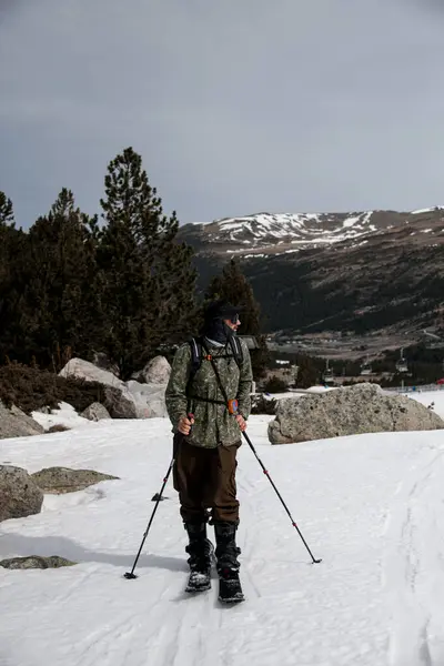 stock image Skier in full gear stands on the snow against the background of a high mountain massif and coniferous trees