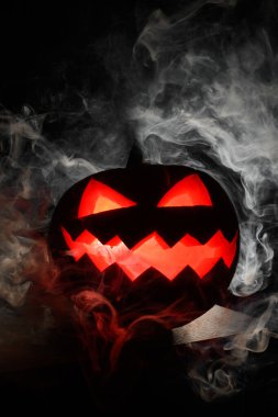 Cadılar Bayramı balkabağı içeriden kırmızı bir fenerle aydınlatılır ve tamamen karanlıkta bir masanın üzerinde dumanla çevrilidir.