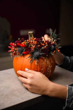 Çiçekçinin dişi elleri masasında yabani çiçek, böğürtlen ve biberden oluşan orijinal bir çiçek düzenlemesini bitirir.