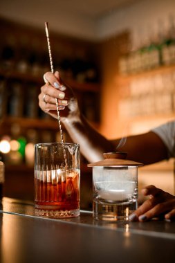 İki bardağın yan görünüşü, biri barmen bir kadının bar kaşığıyla kokteyl karıştırması, diğeri de kapakla kaplanmış ve dumanla dolu.