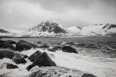 Huzursuz deniz kayalık bir sahilde köpüklü dalgalar kayalara çarpıyor Norveç 'in arka planında hafif karla kaplı.