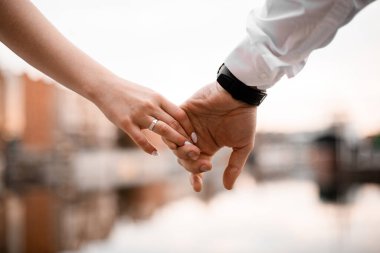 Damatların eli, gelinin elini parmaklarından tutarken, parmaklarından biri, nehrin bulanık arka planına alyans takıyor.