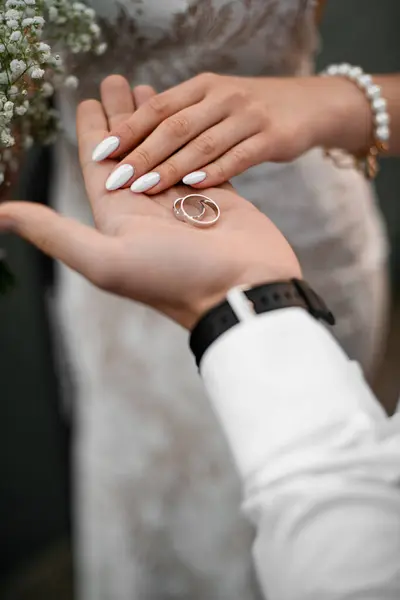 Yakın planda damatların avuç içlerine odaklan. İki alyans ve iki hassas el, bulanık arka planda güzel bir düğün manikürü.