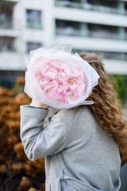 Side view of a pretty girl with a beautiful curly hair in gray jacket with a bouquet of incomparable soft pink flowers in her hands clipart