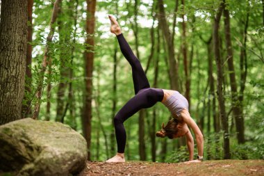 Genç, narin bir kadın köprüde yerde duruyor. Düz bir bacağı var. Arka planda bulanık, seçici bir odak noktası var.