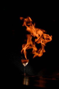 Barmen bardağın arka planında muhteşem bir alev yapıyor, bir kokteyl ile, yanan bir gaz ocağının yanına yanıcı sprey sıkıyor.