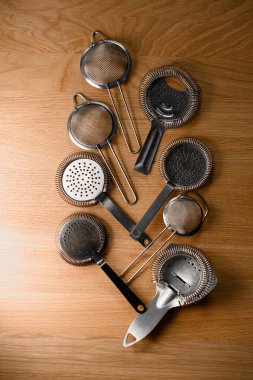 Kokteyl malzemelerini hazırlamak için farklı dikenler ve ince barmen süzgeçleri ringa kemiği şeklinde düz bir tahta yüzeyde yatar.