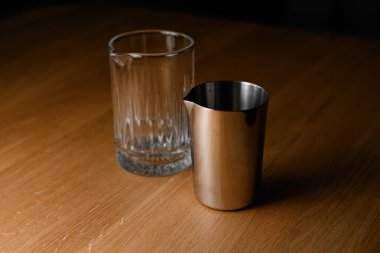 Barmen tarafından ahşap masada kokteyl yapmak için bir bardak ve bir çelik ölçü kabına yakından bakın.