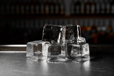 Bulanık bir arkaplanda bir bar tezgahının üzerinde iki katmanlı büyük buz küplerinin yakın plan görüntüsü