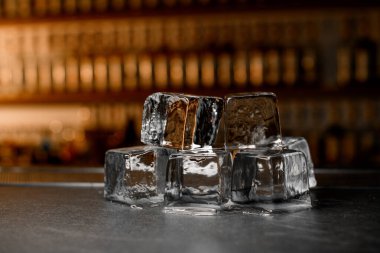 Geniş buz küpleri bir bar tezgahının üzerine uzanır. Işıklandırılmış bir ekranın bulanık arka planında. Ön plana odaklan.