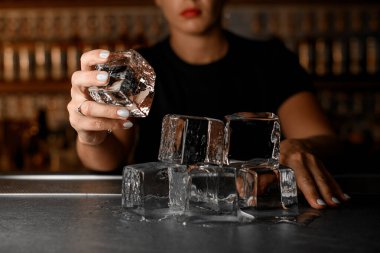 Tezgahın üzerinde yavaşça eriyen büyük buz küpleri var, bunlardan biri de bulanık bir arka planda elinde bir bayan barmen tarafından tutuluyor.