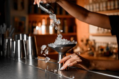 Barmen kadın elleri ezilmiş buz parçalarını bir kepçeyle özel bir tezgaha döker. Böylece bulanık bir arka planda tezgahın üzerine dağılırlar.