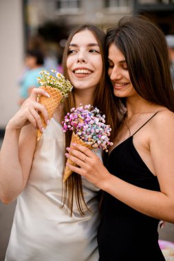 Kızların poz verdiği, kollarını sarmaladığı, içinde güzel çiçek buketleri olan waffle bardakları olan iç açıcı bir an..