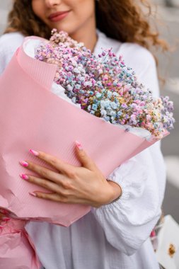 Sevgi dolu kahverengi saçlı bir kız, bir buket çiçeğe sarılıyor..