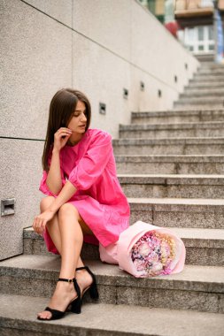 Sessizce oturan pembe elbiseli bir kız güzelliklerinde kaybolmuş, nefes kesen bir buket çiçeğe bakıyor.