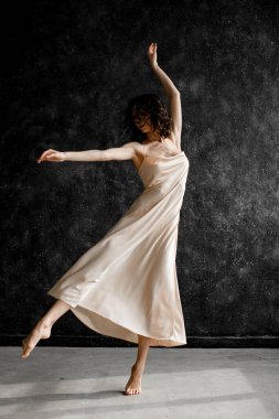 Açık pembe elbiseli zayıf, narin bir kadın, dans eden bale, kolunu ve bacağını bir tarafa hareket ettiren, diğer elini kaldıran, diğer ayağını ayak parmağına kaldıran.