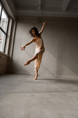 Genç ve güzel dansçı dans stüdyosunda dans hareketleri yapıyor. Sağ bacak ve sol el havaya uzanıyor.