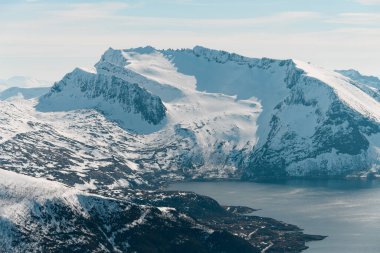 Karla kaplı görkemli kayalık dağlar, ayaklarının dibinde küçük bir nehir, bulutsuz mavi gökyüzünün arka planında.