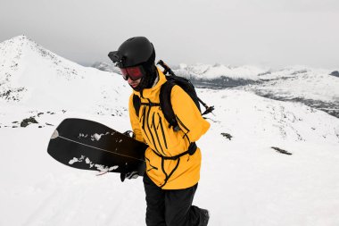 Sarı ceketli tek kollu kayakçının dağlık kış manzarası ve göle karşı bacaklarını tuttuğu yakın plan.