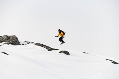 Ekstrem tek kollu kayakçı, bir dağ yamacından geçerken hafif bir gökyüzü arka planına karşı atlama numarası yapar.
