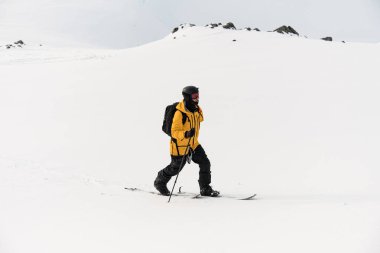 Tek kollu kendine güvenen kayakçı, kayanın bazı kısımlarının karın altından görülebildiği beyaz karlı bir zemine karşı kayak yapıyor.