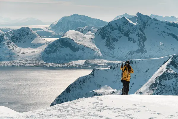 Bir eliyle dağın tepesine tırmanan uzun kayakçı, denizin ve dağların arka planına karşı sonsuz dağ manzaralarına bakıyor, gölün diğer tarafında.