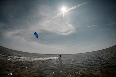 Açık mavi gökyüzü, beyaz bulutlar ve mavi deniz, uzakta mavi bir paraşüt ve uzakta bir sörf tahtasında bir kız.