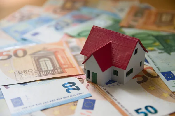 Image of a miniature family house placed on euro banknotes and representing the expenses of the purchase or rent, the mortgage, the notary, the lawyer, the family savings