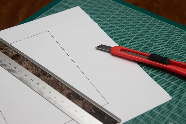 Someone cutting a paper with the help of a cutter and a ruler on a green work table