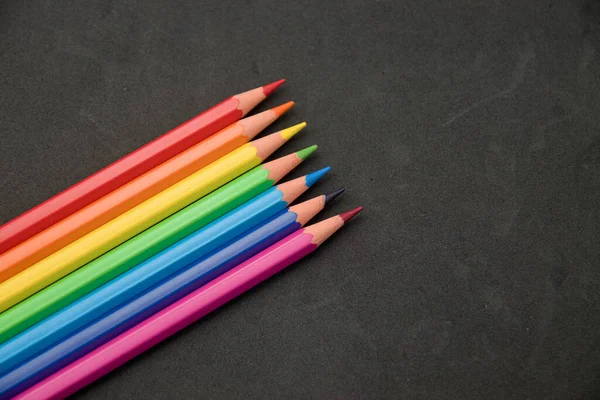 Background for school or artistic content where some colored pencils appear on a textured black surface. Image with copy space.